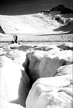 A crevasse on a glacier with researchers and equipment in the background.