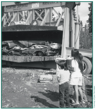 Mentasta students Cynthia Eskilida, Angel Joseph and William Chickelusion watch as cars are crushed for removal from their Village