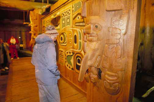 A viewer examines the houseposts in Chief Shakes House