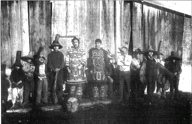 Klukwan villagers stand before the Whale House in dance regalia.