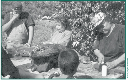 Chester Pence and others watch as Ruby Sinyon and Molly Galbreath, butcher a moose.